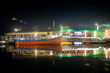 Udaipur, Rajasthan, Hindistan - 26 Ekim 20: Fath Sagar gölünün kenarına park etmiş parlak turuncu teknelerin turist çağıran ışıklarla süslenmiş gece çekimi