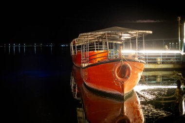 Fateh Sagar gölünün kenarına park etmiş parlak turuncu teknelerin gece çekimleri. Işıklarla süslenmiş turistleri gezmeye çağırıyor.