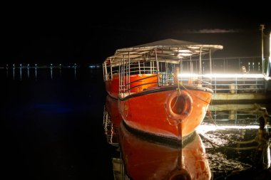 Night shot of bright orange boats parked on the side of Fateh Sagar lake decorated with lights calling tourists for a ride clipart