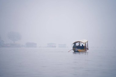 Srinagar Kashmir 'deki Dal Gölü' nde etrafı sislerle çevrili sarı ahşap bir tekne, şehirde turist eksikliğinden dolayı izolasyonu gösteriyor.
