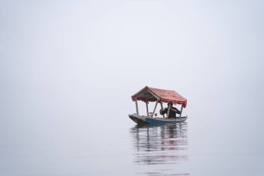 Srinagar, Kashmir - 3 Ocak 2025: Sisli bir günde, Dal Gölü 'nde yüzen kafelerle ünlü Shikara ahşap teknesinde oturan adam