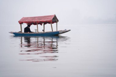 Srinagar, Kashmir - 3 Ocak 2025: Sisli bir günde, Dal Gölü 'nde yüzen kafelerle ünlü Shikara ahşap teknesinde oturan adam