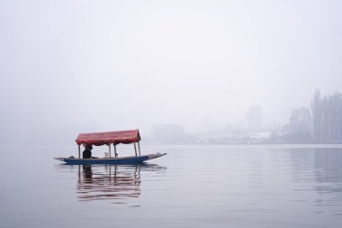 Srinagar, Kashmir - 3 Ocak 2025: Sisli bir günde, Dal Gölü 'nde yüzen kafelerle ünlü Shikara ahşap teknesinde oturan adam