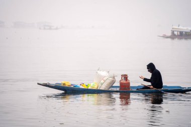Kayıkçı, Srinagar Kashmir 'deki yerel su taşımacılığı merkezli yerel ekonomiyi gösteren dal gölünde gaz silindirleri ve yiyecek maddeleriyle tahta bir kanoda kürek çekiyor.