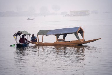 Srinagar, Kashmir - 3 Ocak 2025: Dal Gölü 'ne gelen sınırlı turistler nedeniyle teknelerde başıboş oturan ahşap kayıkçı