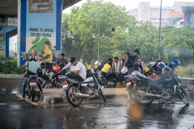 Gurgaon, Delhi, Hindistan - 1 Eylül 2025: Muson yağmurları sırasında uygun bir barınağa sahip olmadıkları için yoğun yağmurda bir köprünün altında duran bisikletler, scooterlar, iki tekerlek