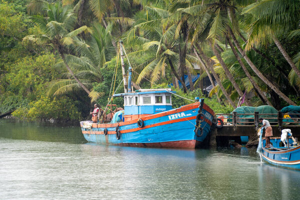 Trucking shot showing the blue deep water fishing boats with the poles and harnesses parked on a riverside jetty in the backwaters during a rain shower