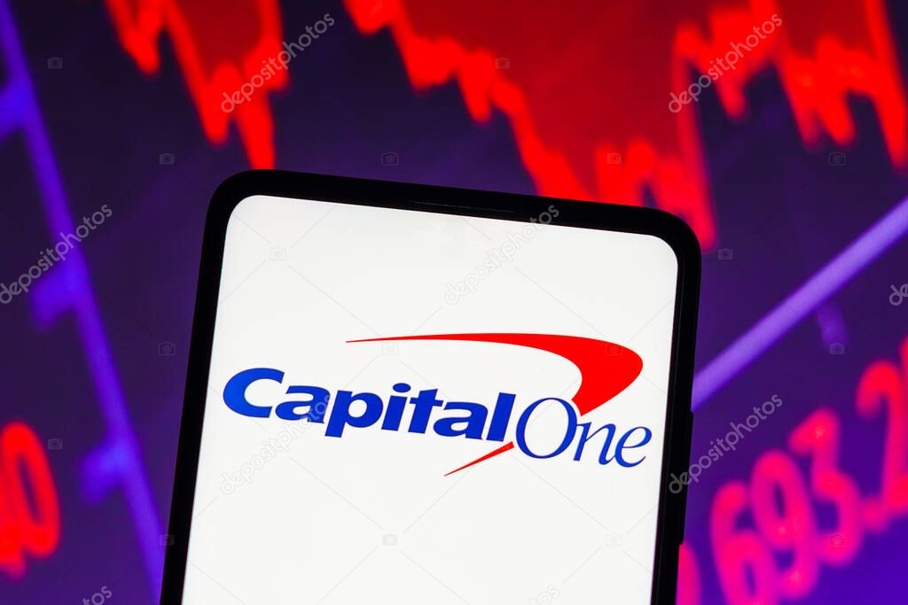 March 15, 2023, Brazil. In this photo illustration the Capital One Financial Corp. logo seen displayed on a smartphone screen, with graphic representation of the stock market in the background