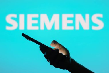 13 Haziran 2023, Brezilya. Bu resimde Siemens logosu arka planda cep telefonu tutan siluet bir kadının logosu görülüyor.