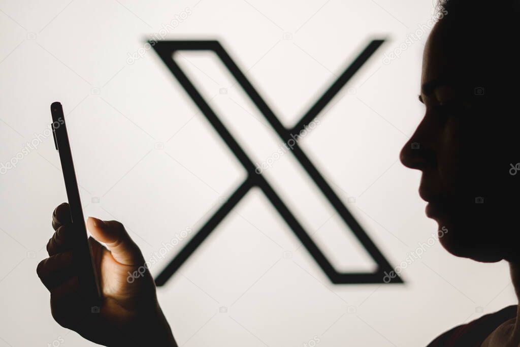 July 24, 2023, Brazil. In this photo illustration, a woman's silhouette holds a smartphone with the Twitter (X) new logo in the background