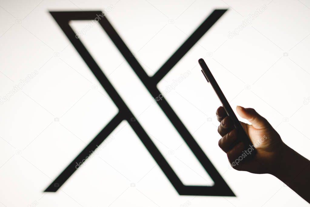 July 24, 2023, Brazil. In this photo illustration, a woman's silhouette holds a smartphone with the Twitter (X) new logo in the background