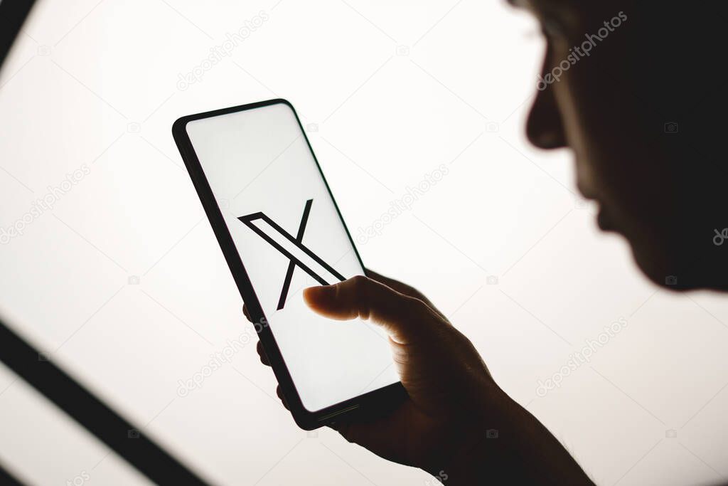 July 24, 2023, Brazil. In this photo illustration, a silhouetted woman holds a smartphone with the Twitter (X) new logo displayed on the screen