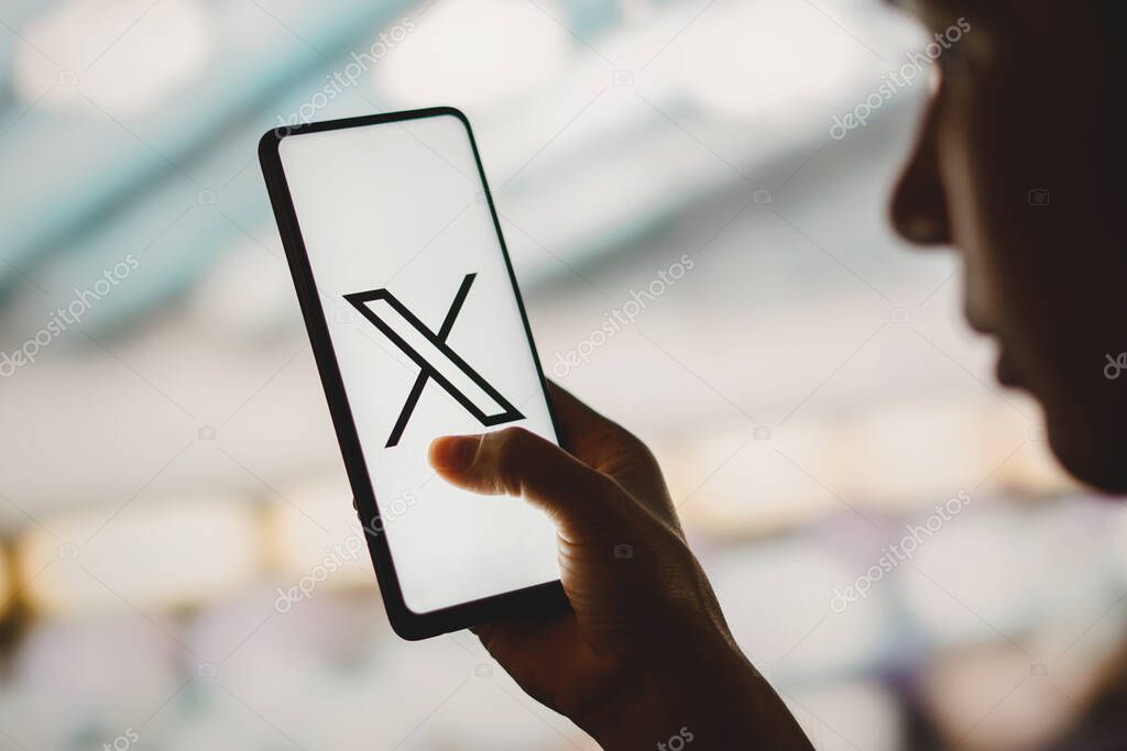 July 24, 2023, Brazil. In this photo illustration, a silhouetted woman holds a smartphone with the Twitter (X) new logo displayed on the screen