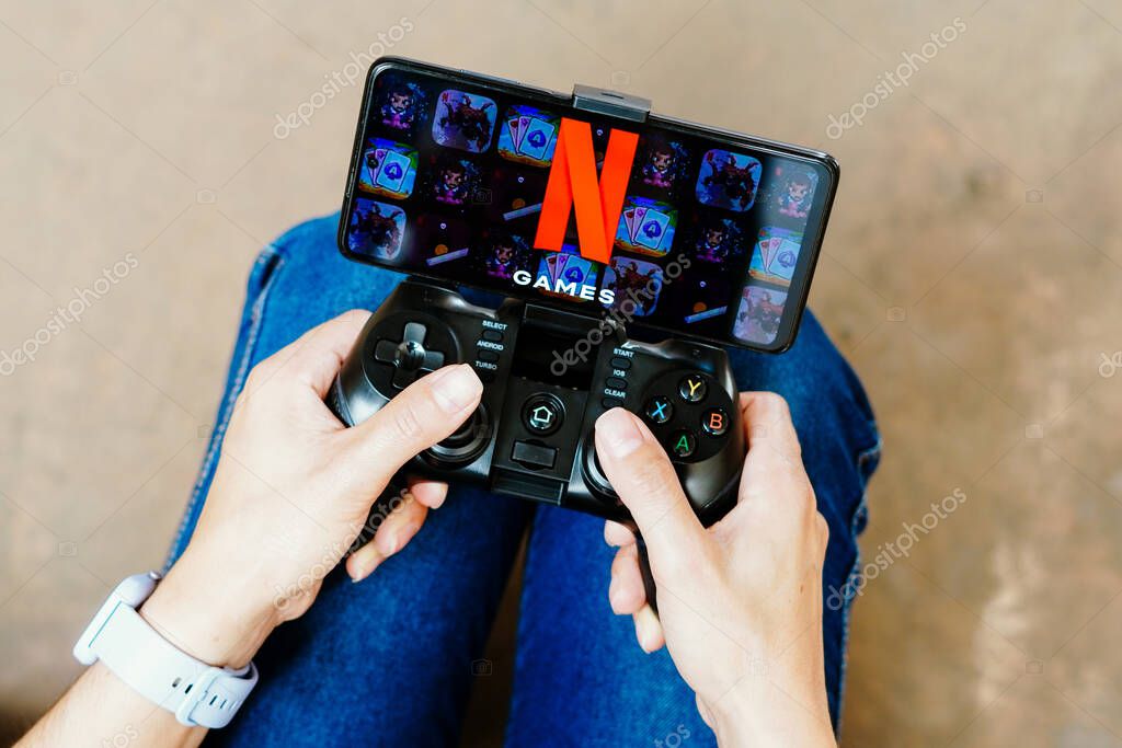 August 8, 2023, Brazil. In this photo illustration, a person playing on a joystick and the Netflix Games logo displayed on a smartphone screen