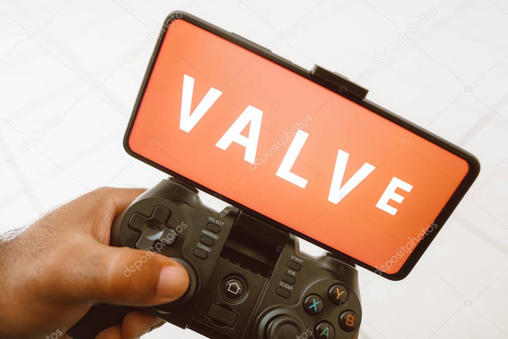 August 11, 2023, Brazil. In this photo illustration, a person plays on a joystick and the Valve Corporation logo displayed on a smartphone screen