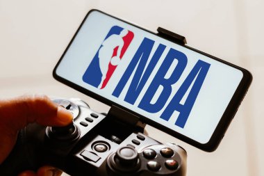 15 Ağustos 2023, Brezilya. Bu resimde, bir kişi bir oyun kumandasında oynuyor ve Ulusal Basketbol Birliği (NBA) logosu akıllı telefon ekranında sergileniyor.
