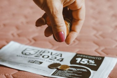 December 12, 2023, Brazil. In this photo illustration, a woman counts the real money coins and, on top of the IPVA (Imposto sobre a Propriedade de Veculos Automotores) payment slip. clipart