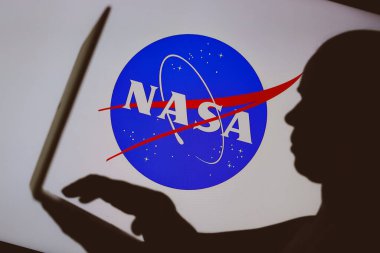 9 Ocak 2024, Brezilya. Bu resimde, Ulusal Havacılık ve Uzay İdaresi (NASA) logosu defter kullanan bir kişinin siluetinin arka planında görülmektedir.