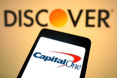 19 Şubat 2024, Brezilya. Bu resimde, Capital One Financial logosu arka planda Discover Financial Services logosu olan bir akıllı telefon ekranında sergilenmektedir. Capital One 'ın Discover' ı ele geçirmek için görüştüğü söyleniyor. Önerilen d