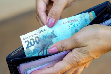 19 Nisan 2024, Brezilya. Bir kadın cüzdanında 200 reais (200 reais) bulundurur. Resmi verilere göre, kişi başına düşen ortalama hane geliri (kişi başına) Brezilya 'da ayda 1.848 dolara yükseldi..