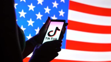 Brezilya - 26 Nisan 2024: Ekranda TikTok logosu ve arka planda ABD bayrağı bulunan akıllı telefonu tutan kadın.
