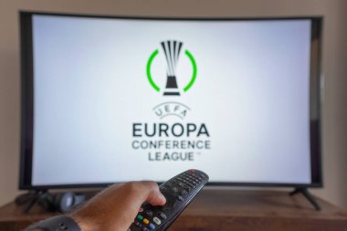14 Mayıs 2024, Brezilya. Bu resimde, TV ekranında UEFA Avrupa Konferans Ligi (UECL) logosu önünde uzaktan kumandayı tutan bir el görülüyor.