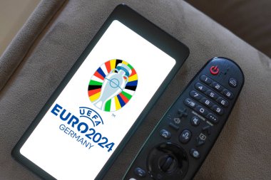 20 Mayıs 2024, Brezilya. Bu fotoğraf illüstrasyonunda, UEFA Avrupa Futbol Şampiyonası (Euro 2024 Almanya) logosu bir televizyon uzaktan kumandasının yanında bir akıllı telefonda sergilenmektedir. Avrupa coun 'dan erkekler takımları arasındaki ana futbol şampiyonası.