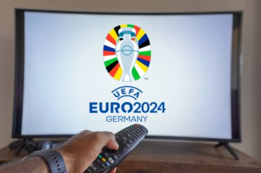 20 Mayıs 2024, Brezilya. Bu resimde, bir televizyon ekranında UEFA Avrupa Futbol Şampiyonası (Euro 2024 Almanya) önünde uzaktan kumandayı tutan bir el görülüyor.