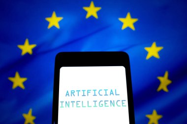 21 Mayıs 2024, Brezilya. Bu fotoğraf illüstrasyonunda, Yapay Zeka (AI) metni akıllı telefon ekranında ve arka planda Avrupa Birliği bayrağı gösterilir. AB Konseyi, AI Yasasını çığır açan bir yönetmeliği onayladığını açıkladı.