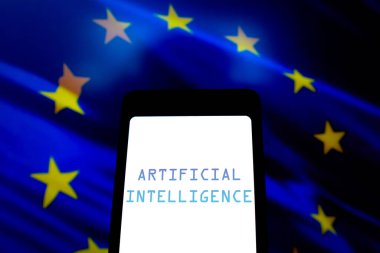 21 Mayıs 2024, Brezilya. Bu fotoğraf illüstrasyonunda, Yapay Zeka (AI) metni akıllı telefon ekranında ve arka planda Avrupa Birliği bayrağı gösterilir. AB Konseyi, AI Yasasını çığır açan bir yönetmeliği onayladığını açıkladı.
