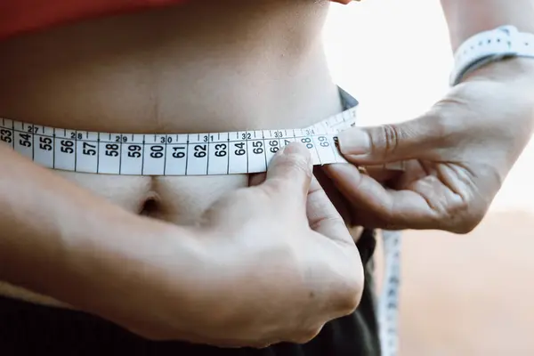 stock image July 1, 2024, Paraguay. In this photo illustration, a woman takes her waist measurements with a measuring tape. According to the World Health Organization (WHO), 12.5% of the world's population is considered obese.