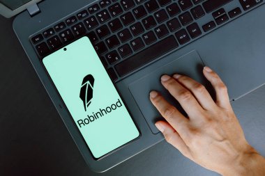 21 Temmuz 2024, Paraguay. Bu fotoğraf illüstrasyonunda Robinhood Marketleri, Inc. logosu, dizüstü bilgisayar kullanan bir kişinin yanındaki akıllı telefon ekranında sergilenmektedir.