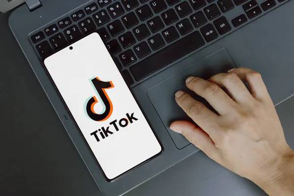 stock image July 21, 2024, Paraguay. In this photo illustration, the TikTok logo is displayed on a smartphone screen next to a person using laptop