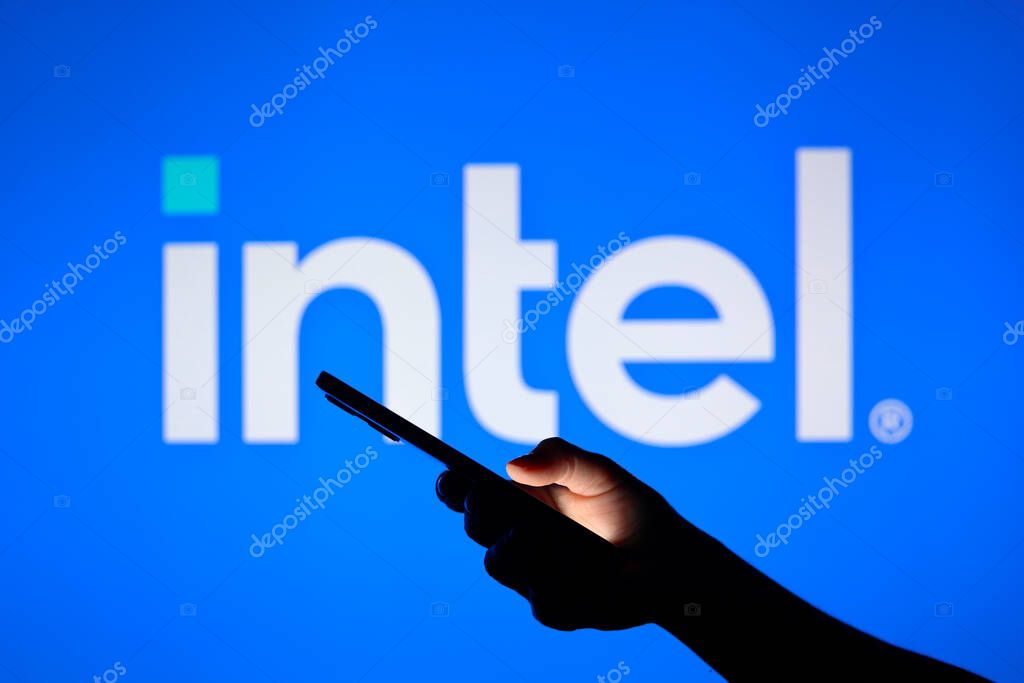 August 3, 2024, Paraguay. In this photo illustration, the Intel Corporation logo seen in the background with a silhouette hand holding a smartphone