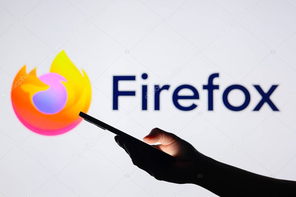 August 15, 2024, Paraguay. In this photo illustration, the Mozilla Firefox logo seen in the background with a silhouette hand holding a smartphone