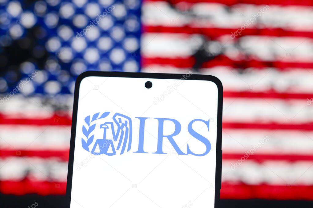 August 15, 2024, Paraguay. In this photo illustration, the Internal Revenue Service (IRS) logo is displayed on a smartphone screen and in the background the flag of the United States of America (USA)