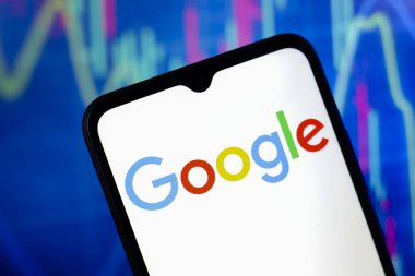 Google logosu akıllı telefon ekranında ve arka planda, ABD 'nin Reno şehrinde 15 Kasım 2024' te bilgisayar ekranında bir borsa grafiği gösterilir.