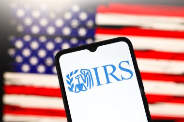 Vergi Dairesi (IRS) logosu bir akıllı telefonun ekranında ve arka planda Amerika Birleşik Devletleri bayrağı 3 Aralık 2024 'te Reno, ABD' de bilgisayar ekranında görünür.