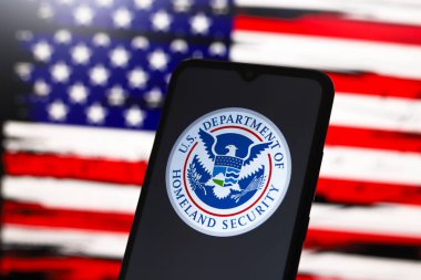 ABD İç Güvenlik Bakanlığı (DHS) logosu bir akıllı telefon ekranında ve arka planda ABD bayrağı 3 Aralık 2024 'te Reno, ABD' de bilgisayar ekranında görünür.