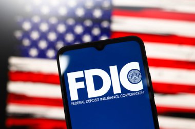 ABD Federal Mevduat Sigorta Şirketi (FDIC) logosu bir akıllı telefon ekranında ve arka planda ABD bayrağı 3 Aralık 2024 'te Reno, ABD' de bilgisayar ekranında görünür.