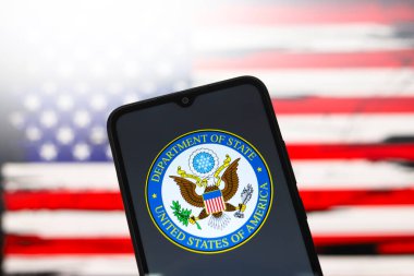 The United States Department of State (DOS) logo appears on the screen of a smartphone and in the background the flag of the United States on the computer screen, in Reno, United States, on December 3, 2024 clipart