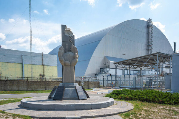 Chernobyl, Ukraine - Aug 07, 2019: Monument to professionals who protected the world from nuclear disaster and Reactor 4 New Safe Confinement - Chernobyl Exclusion Zone, Ukraine