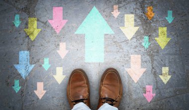 Kahverengi deri ayakkabılar ve zıt yönlerde renkli tebeşirli oklar zorluk kavramına karşı.