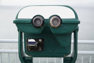 Madeni paralar üzerinde yeşil turist dürbünü ve ikinci planda çözünmüş deniz