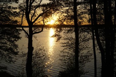 Gölün üzerinde gün batımı ve kıyıda ağaçlar