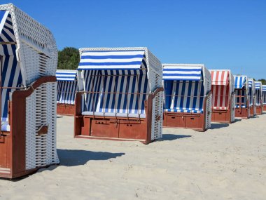 Geniş, güneşli bir kumsalda, açık mavi gökyüzünün altında geleneksel Alman Strandkorb plaj sandalyelerinin düşük açılı bir görüntüsü..