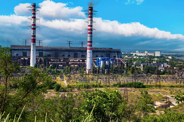 Smoking chimneys of a thermal power plant providing electricity to the city. Smoke pipes. Thermal power plant. Industrial building. Energy production. Blue sky with white clouds.