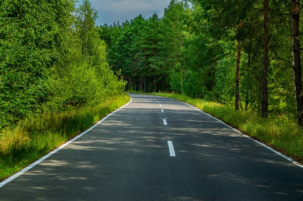 stock image Two-lane asphalt road with white markings in the forest. Asphalt pavement. Road white markings. Place for car traffic. Forest trees. Autotourism and travel. Highway turn. The beauty.