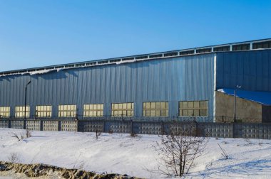 Pencereli paslanmaz çelikten yapılmış endüstriyel bir bina. Fabrikanın üretim atölyesi. Endüstriyel bina. Paslanmaz çelik. Cam pencereler. Kış mevsimi. Mavi gökyüzü. Sanayi.