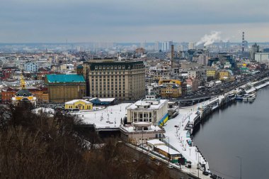 Bulutlu ufku olan Kiev Ukrayna şehri. Kiev Podil Bölgesi. Evler ve sanayi binaları. Gökyüzü ve ağaçlar. Dnepr Nehri. Otoyol. Kış mevsimi. Beyaz kar. Kuş bakışı bir bakış açısından..